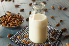 A bottle of almond milk surrounded by almonds on a wooden surface